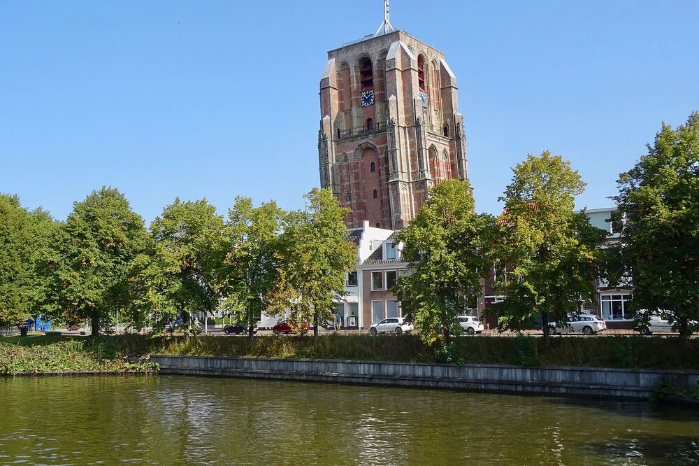 De scheve toren Oldehove in Leeuwarden gezien over het water, met bomen langs de kade
